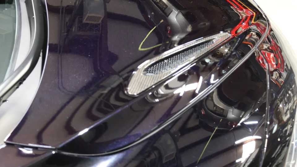 Close-up detail of a dark purple McLaren's carbon fiber fender vent, showcasing the glossy finish.