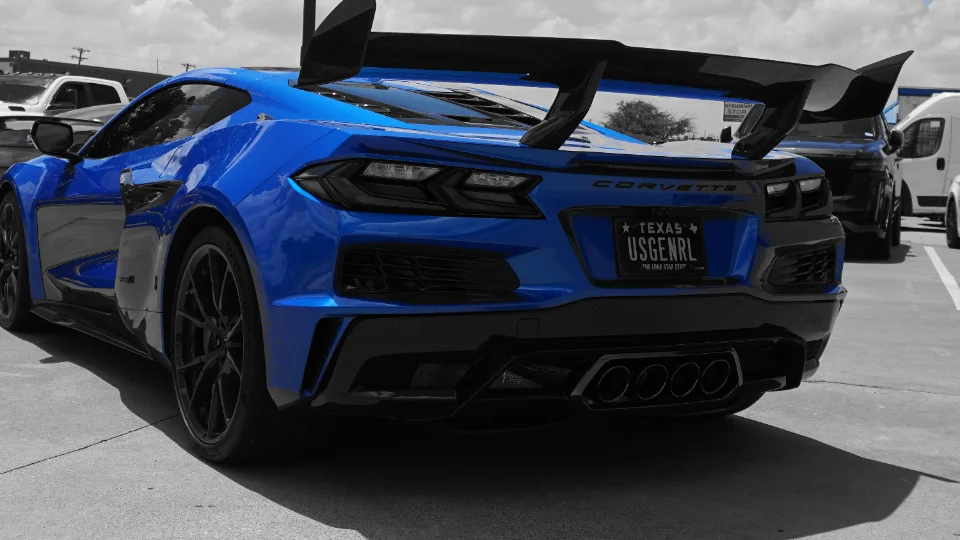 A blue C8 Corvette with a large rear wing and quad exhaust tips parked outdoors.