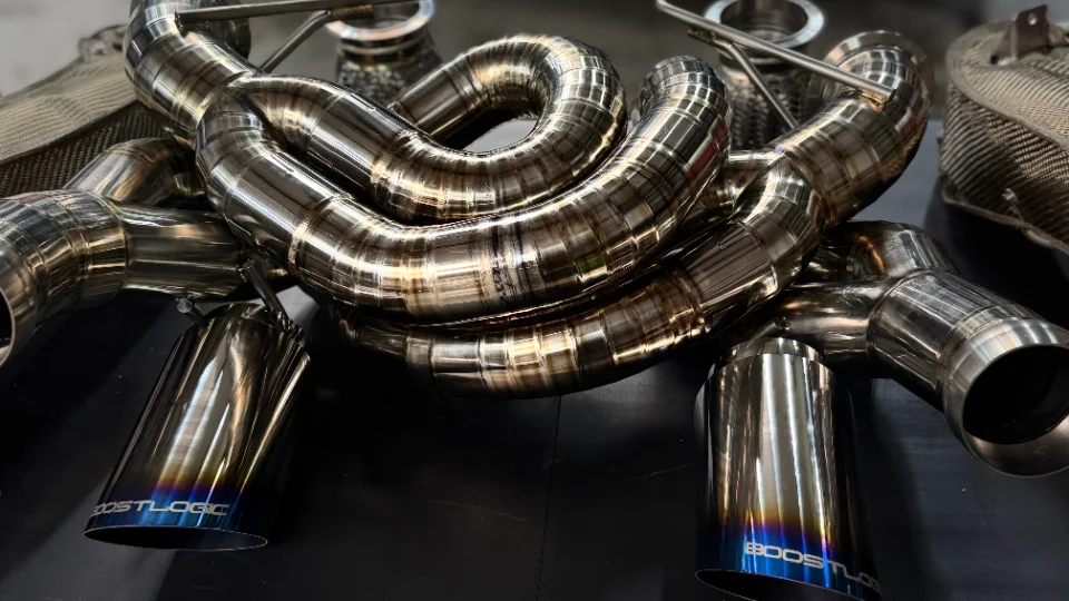 Close-up of a Boost Logic titanium exhaust system with burnt tips, showcasing intricate piping and welds.
