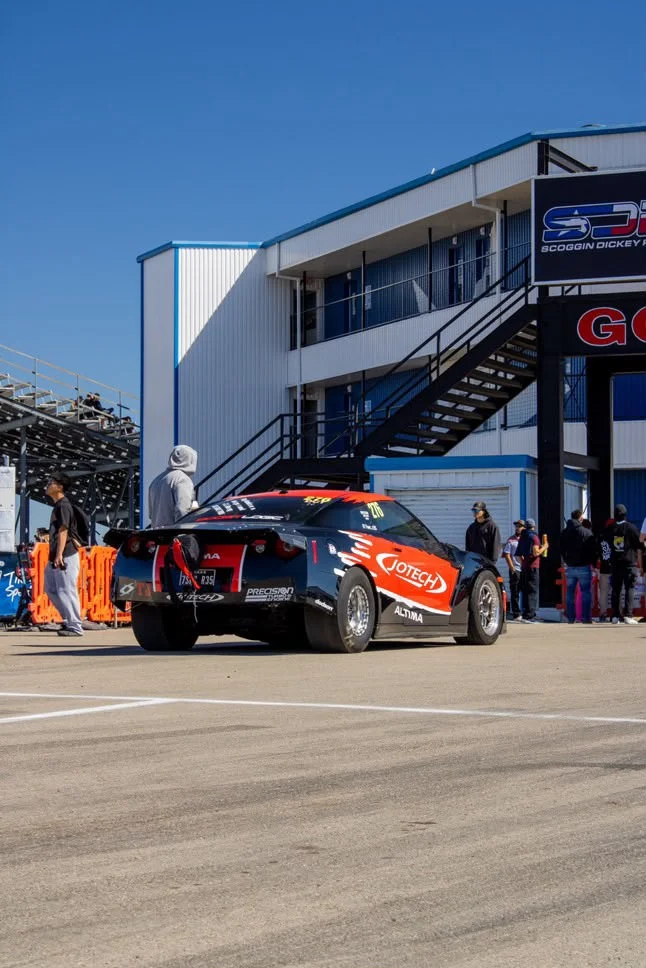 A black and red Jotech Nissan GT-R drag car with a parachute at the rear, staged on a drag strip with a building in the background.