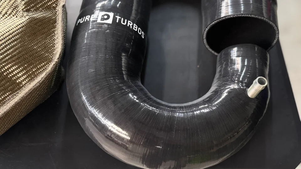 Close-up of a Pure Turbos silicone boost hose next to a heat shield, showcasing performance engine components.