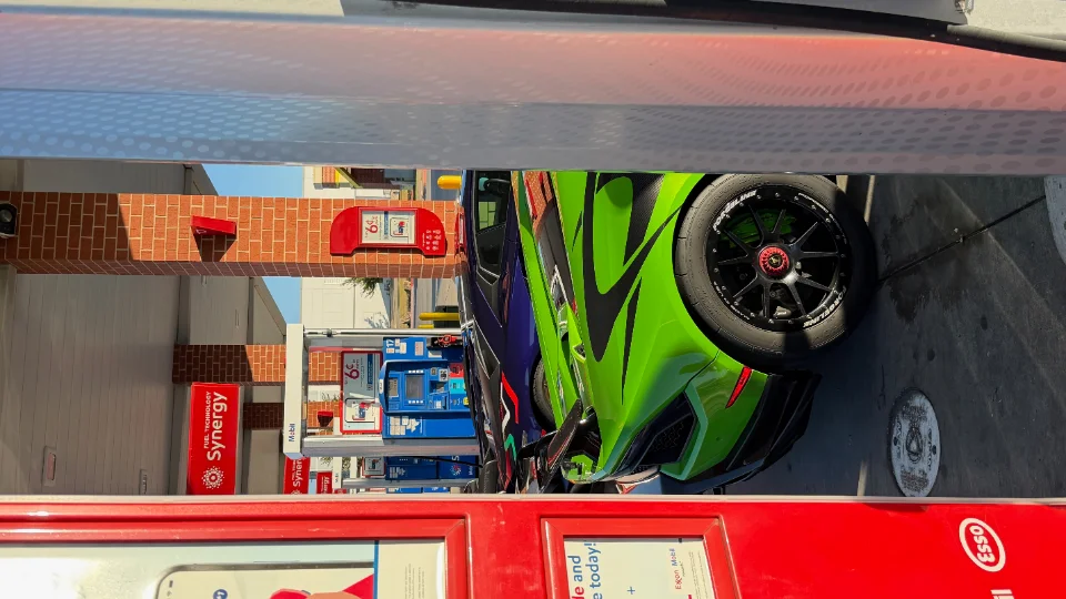 A vibrant green Lamborghini with black Forgeline wheels at a gas station, showcasing its aggressive styling.
