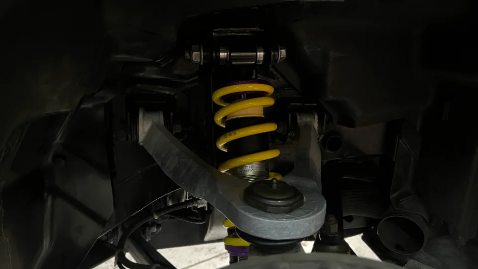 Close-up view of a car's suspension system, featuring a yellow coilover spring and associated chassis components.