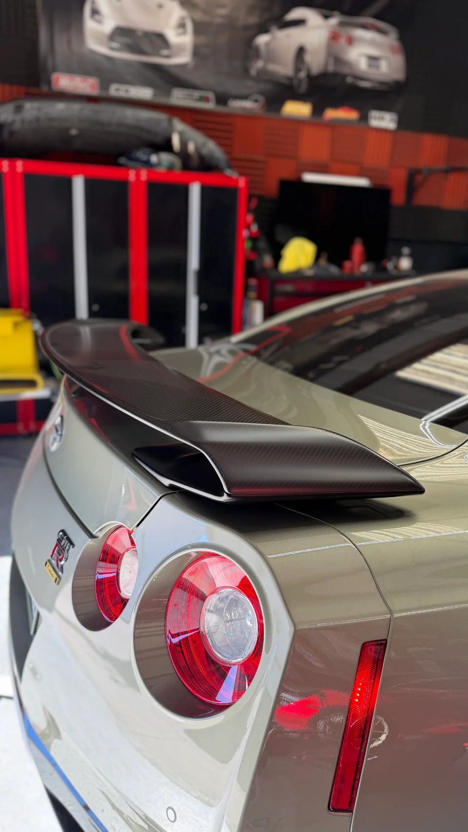 Close-up of a Nissan GT-R's rear with a carbon fiber wing and round LED tail lights in a performance shop.