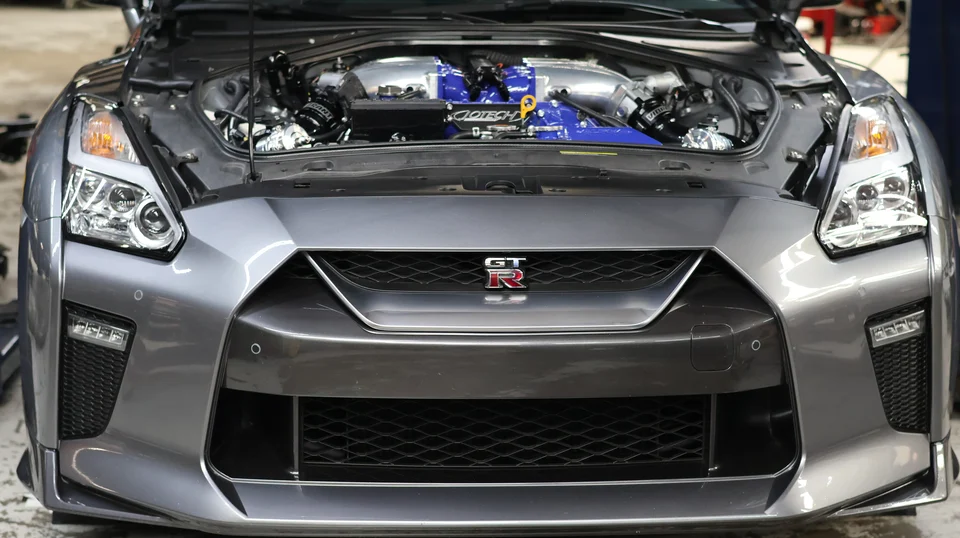 Front view of a grey Nissan GT-R with its hood open, revealing a high-performance engine bay with a blue aftermarket induction system.