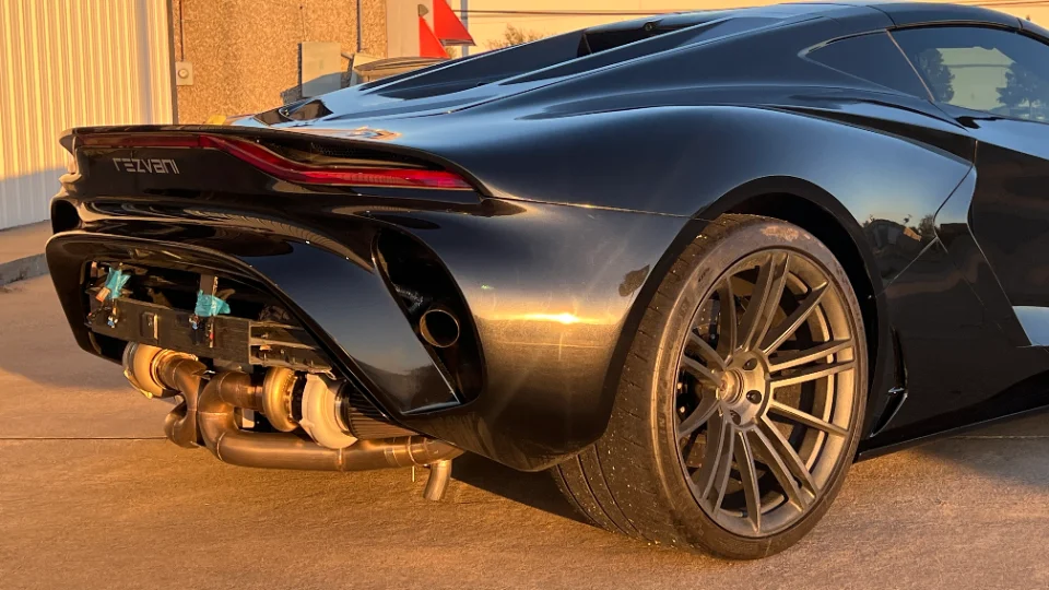 Rear view of a black Rezvani supercar with its bumper removed, exposing twin turbochargers and custom exhaust system.