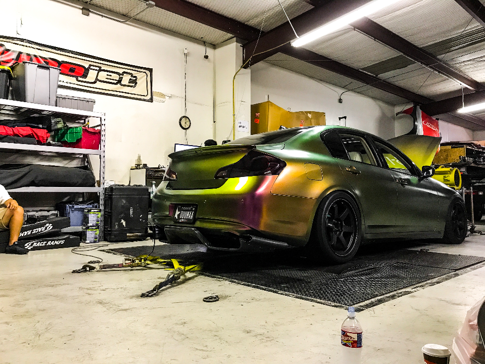 A chameleon-wrapped Infiniti G37 sedan strapped to a dyno for performance tuning at a Jotech Motorsports shop.
