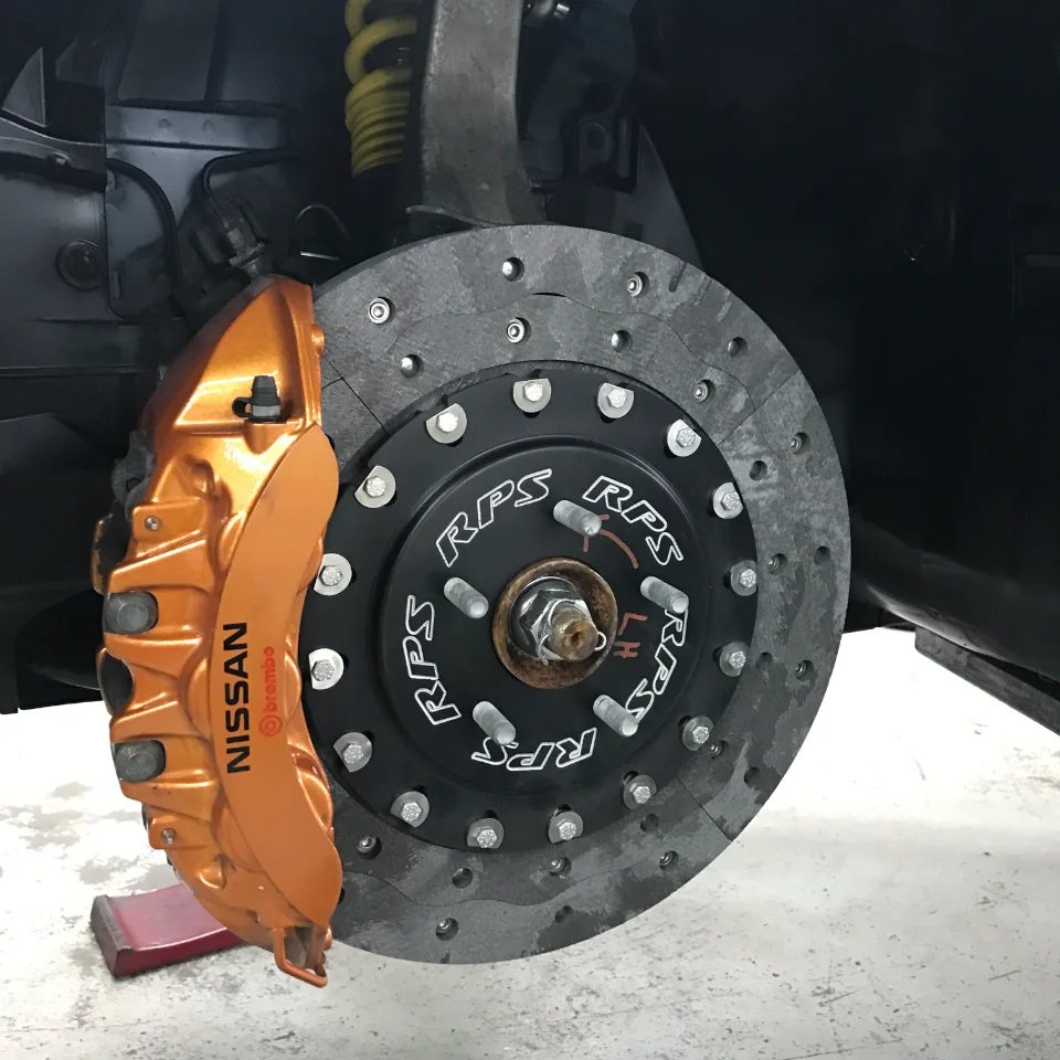 Close-up of a Nissan GT-R's orange Brembo brake caliper and RPS carbon ceramic rotor with suspension visible.