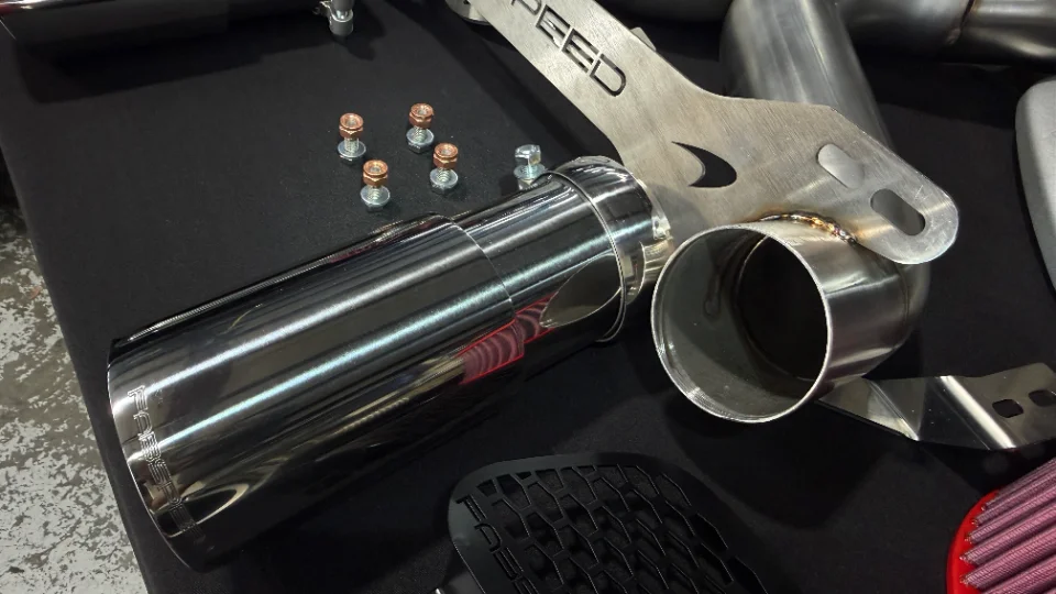 Close-up of performance exhaust components including a chrome tip, stainless steel piping, and an air filter.