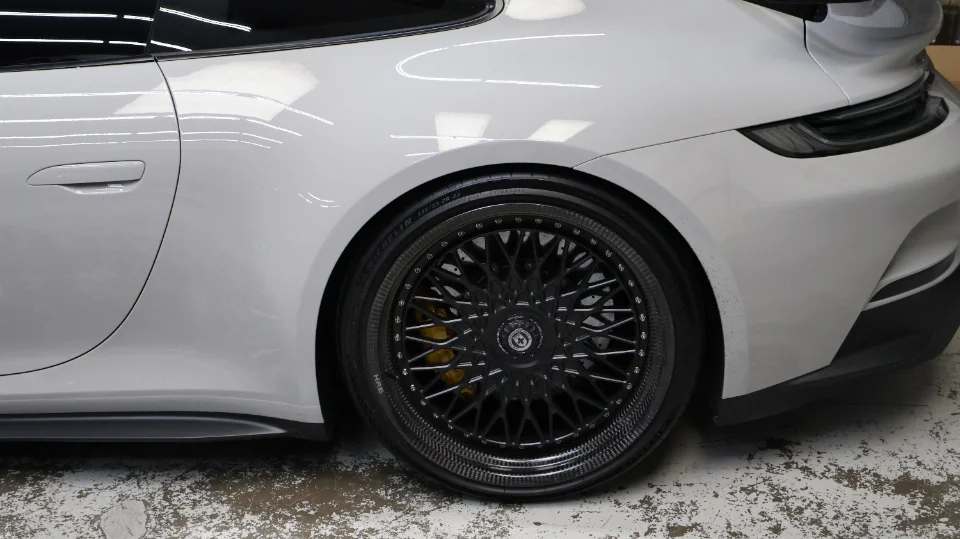 A white Porsche with black HRE custom wheels featuring carbon fiber barrels and yellow brake calipers.