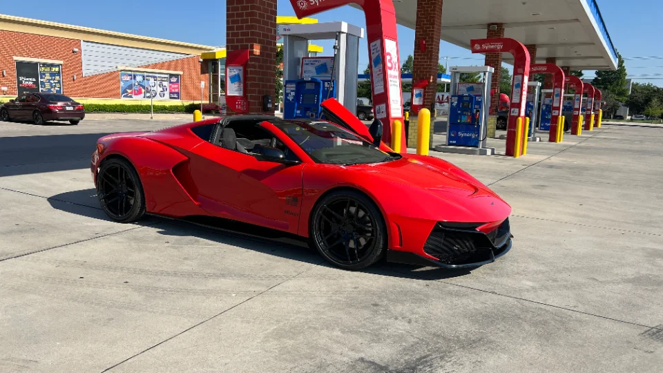 A striking red custom sports car with black aftermarket wheels parked at a gas station on a bright, sunny day.