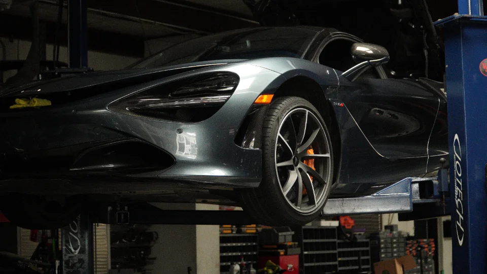 A grey McLaren 720S sports car elevated on a blue car lift inside a Jotech Motorsports performance tuning shop.