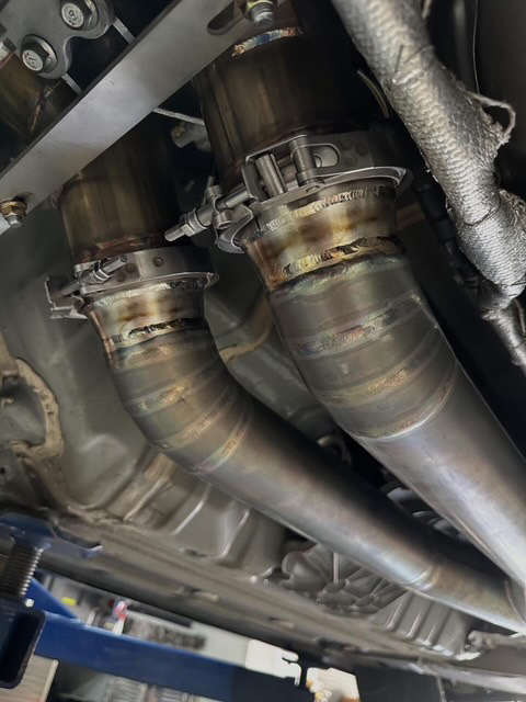 Custom exhaust system with v-band clamps installed under a performance car in a shop.
