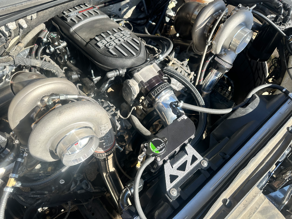 Close-up of a highly modified engine bay featuring twin turbochargers, a Boss 302 intake manifold, and custom boost piping.
