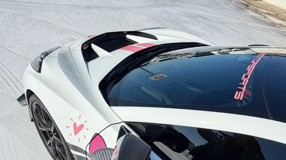 A white McLaren supercar with pink racing stripes and heart decals parked in a snowy landscape, showcasing its custom exterior.