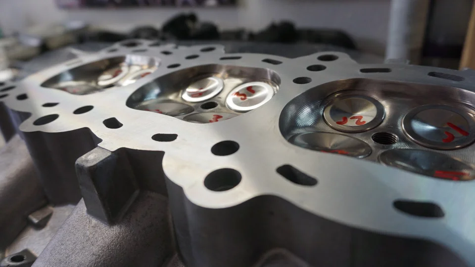 Close-up of a performance engine cylinder head with valves, marked for assembly or porting