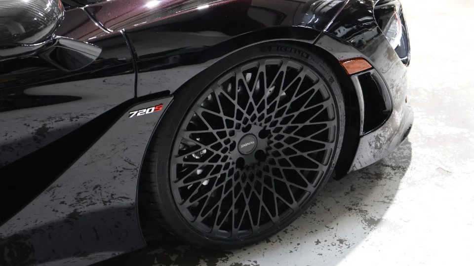 Close-up of a black McLaren 720S featuring custom Signal wheels and performance tires, highlighting the intricate wheel design.