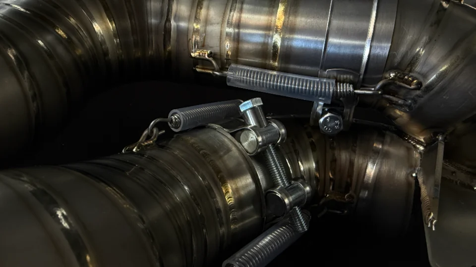 Close-up of a performance exhaust system with visible welds and springs, showcasing fabrication details.