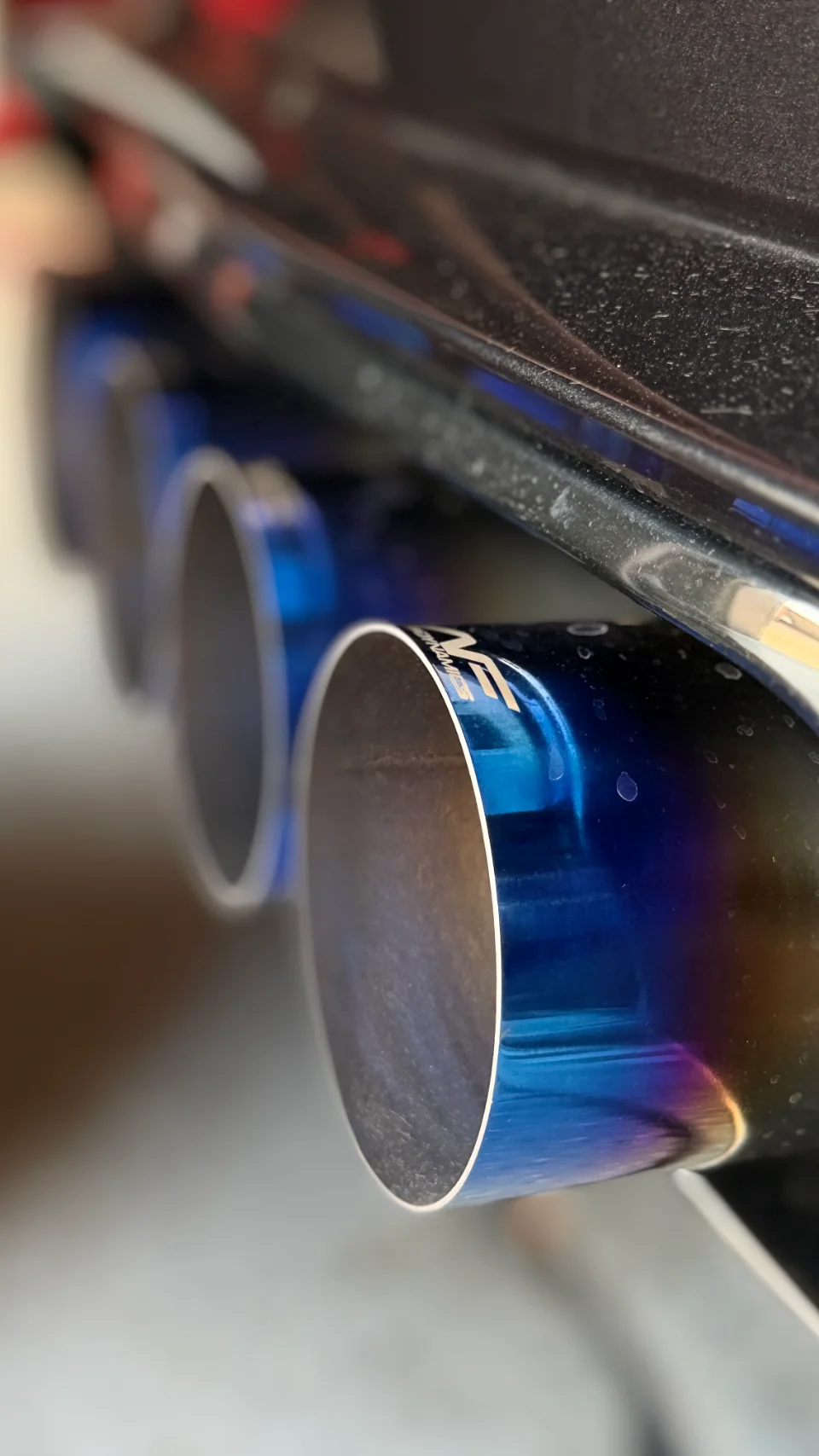 Close-up of aftermarket blue and purple burnt titanium exhaust tips on a performance car.