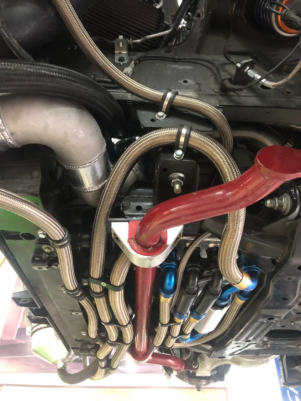 Detailed view of a car's underside showing custom braided lines, AN fittings, and boost piping for performance upgrades.