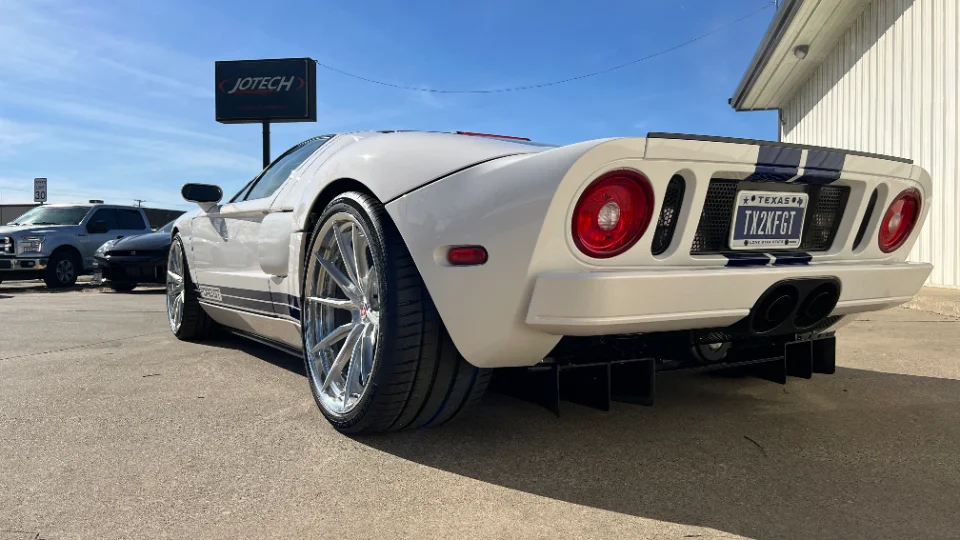 White Ford GT with blue racing stripes, aftermarket wheels, and a rear diffuser parked outside Jotech Motorsports.