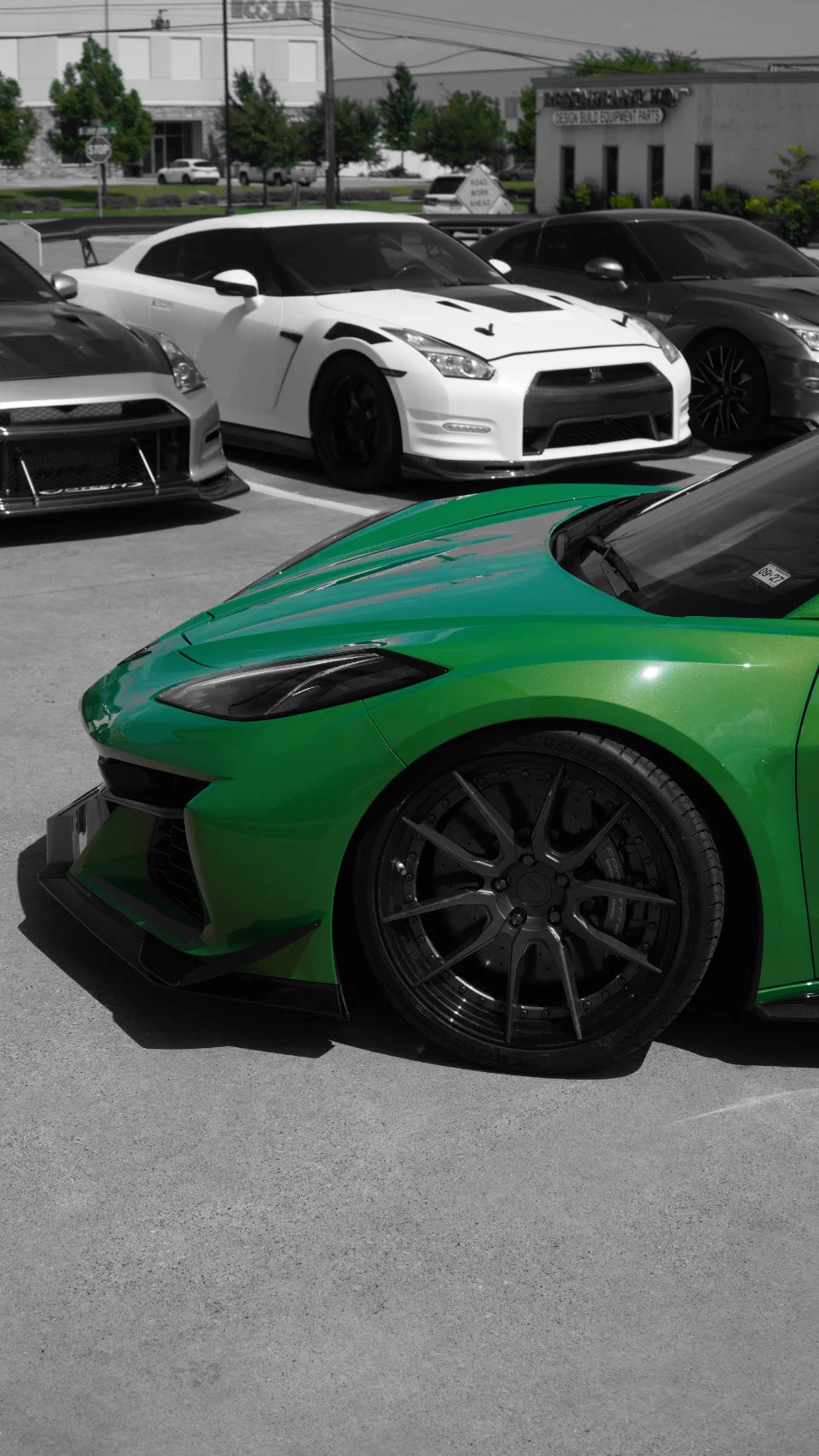 A vibrant green Corvette C8 with custom wheels and a front splitter parked alongside two Nissan GT-Rs in a parking lot.