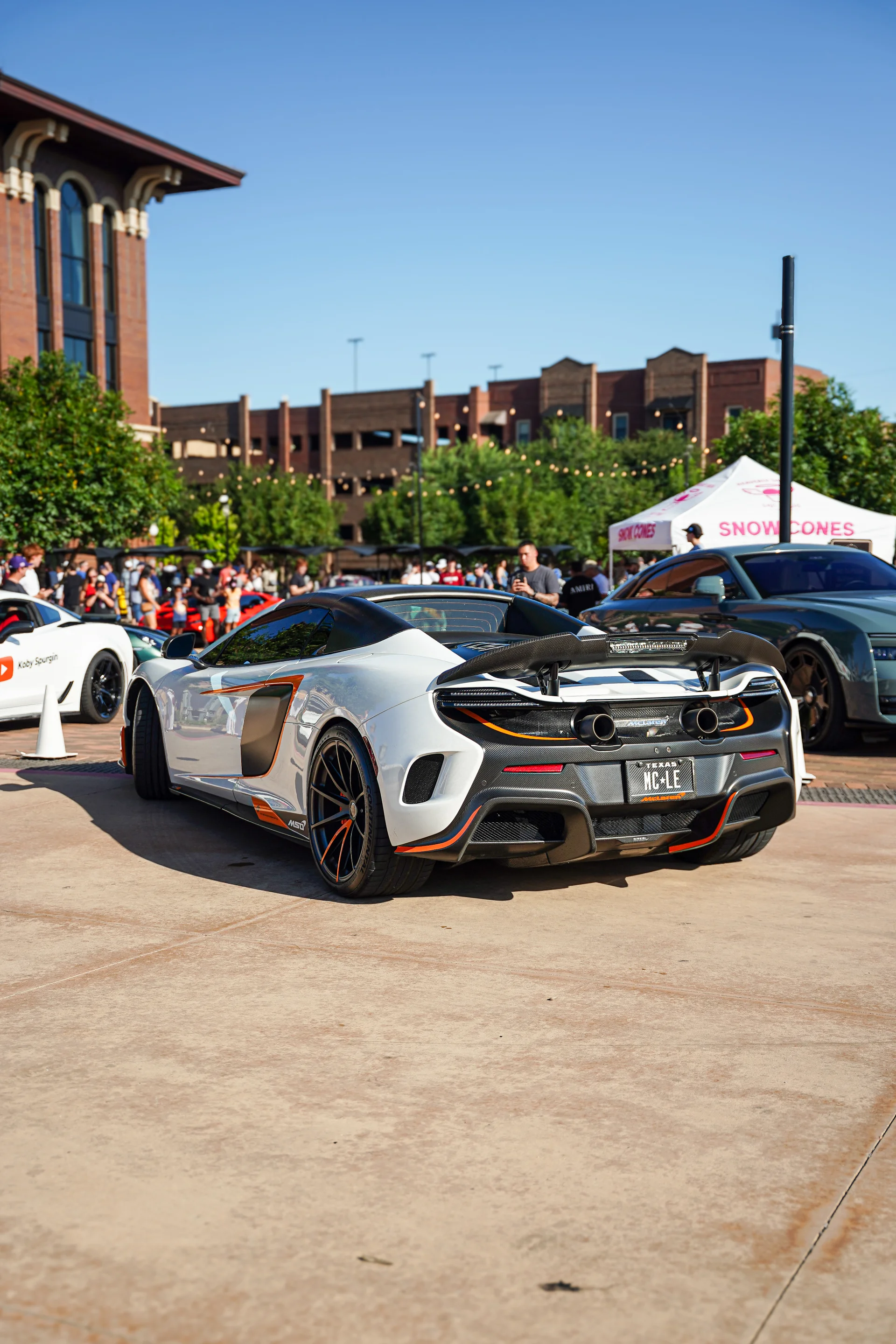 A white McLaren 600LT with carbon fiber aero and custom wheels parked at an outdoor car show.