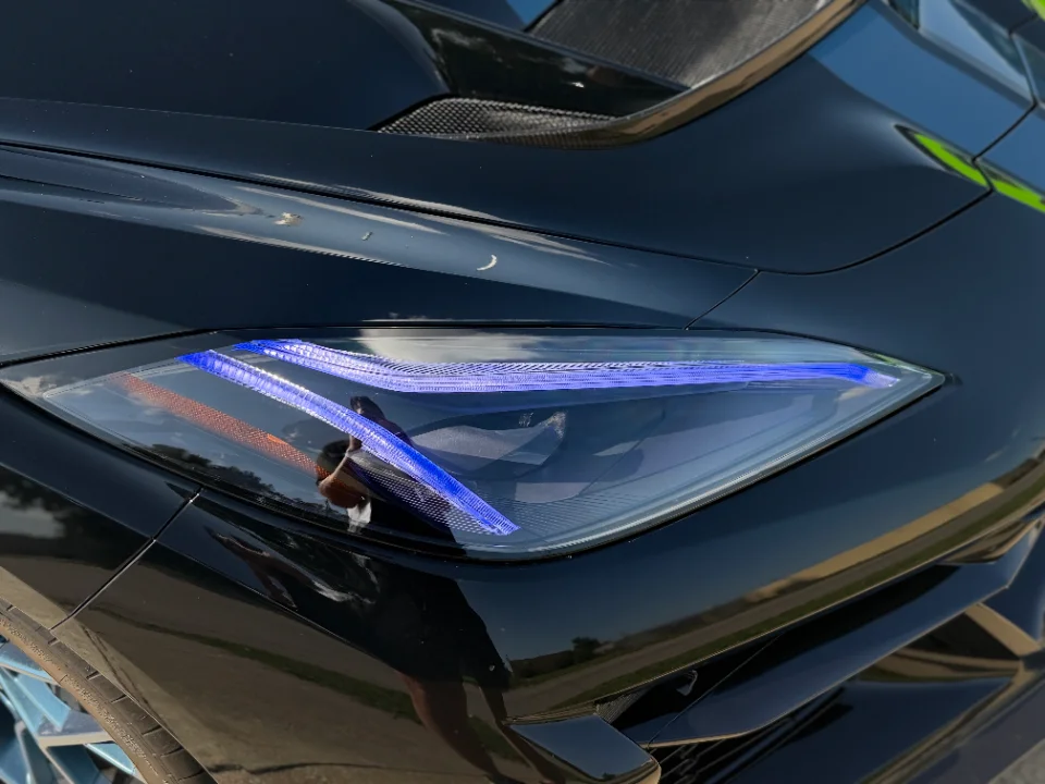Close-up detail of a black C8 Corvette's front headlight with blue LED daytime running lights.