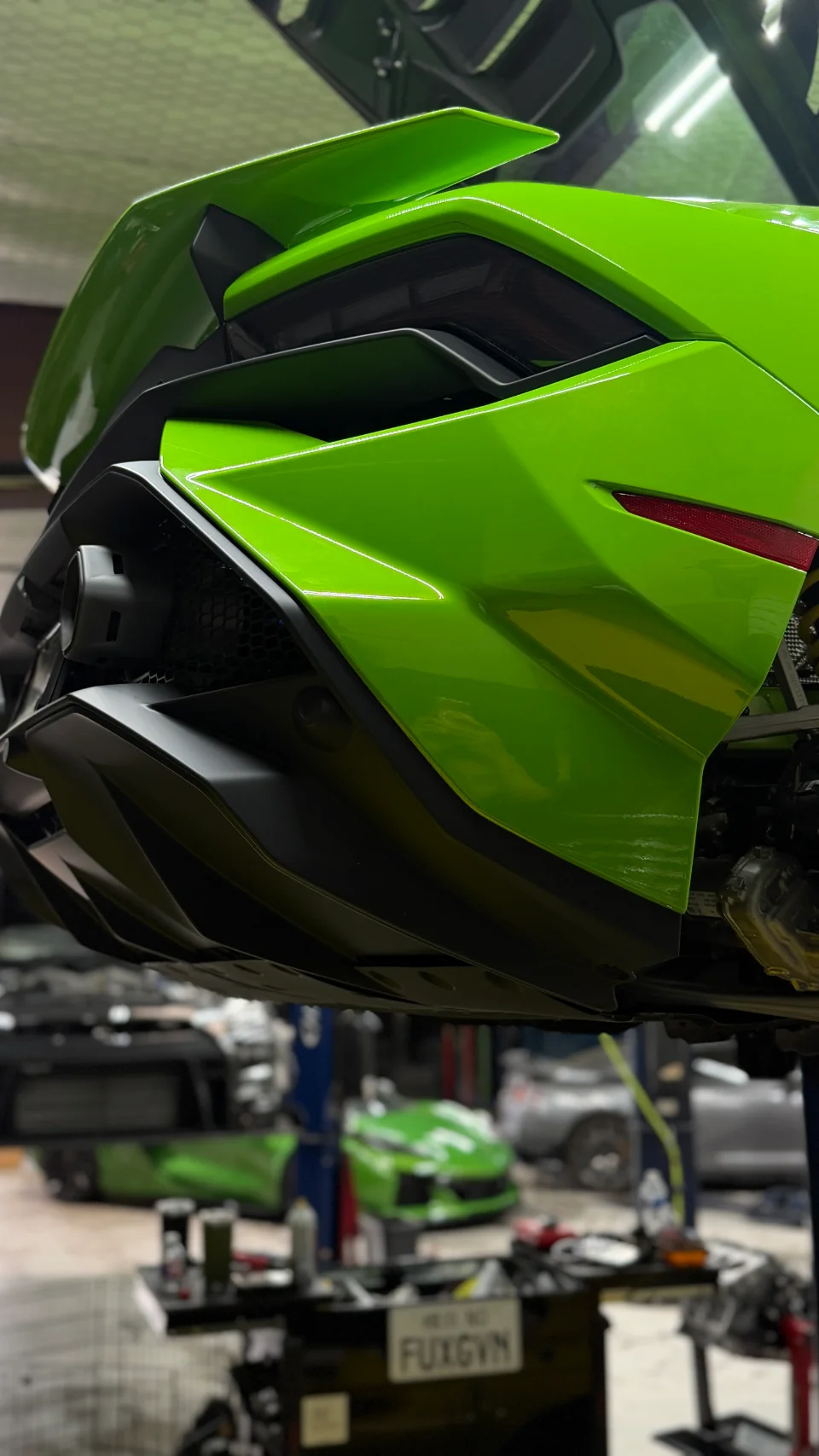 Rear view of a green Lamborghini Huracan on a lift in a performance shop, showcasing the diffuser and exhaust.