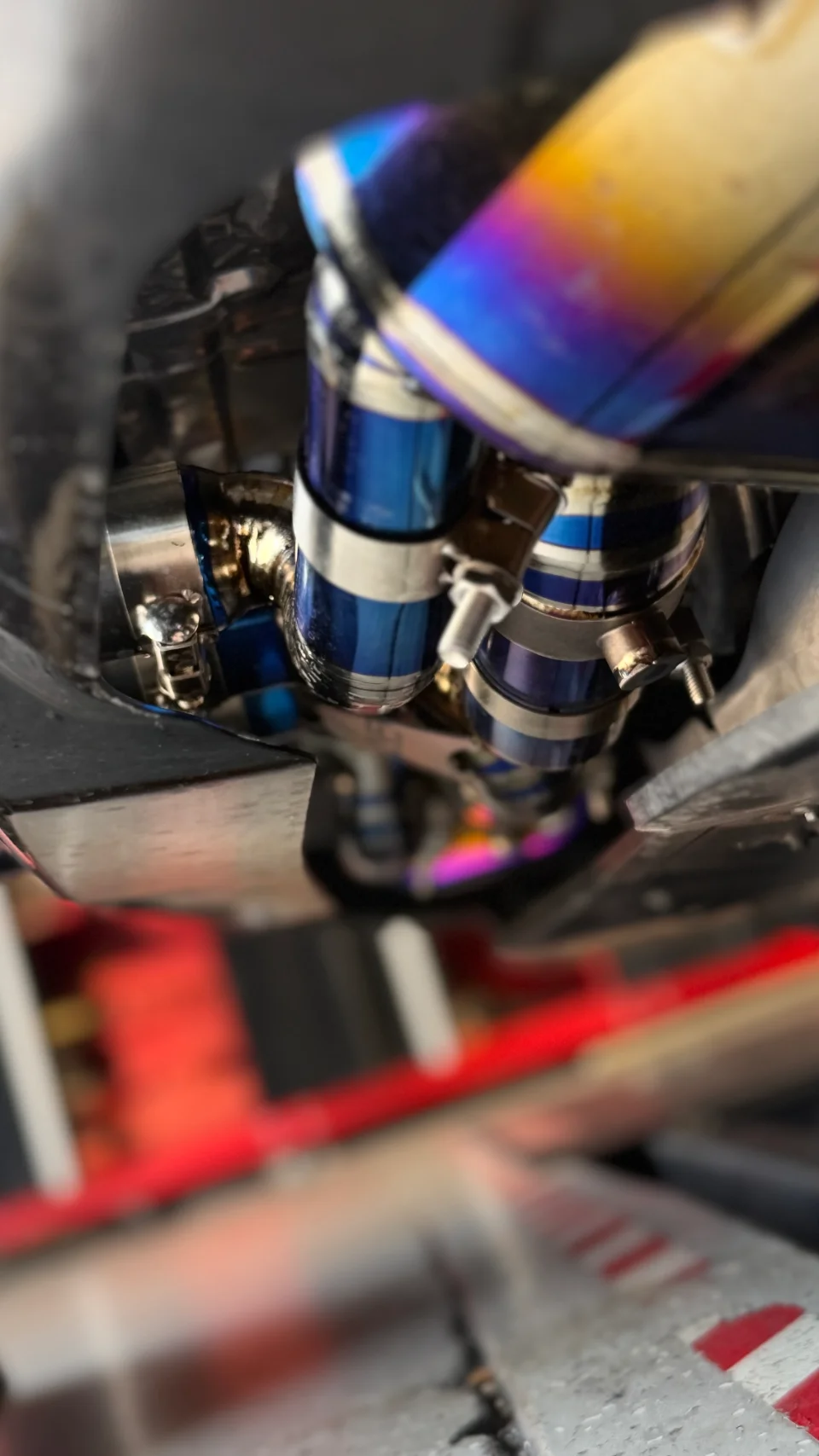 Close-up view of a performance exhaust system featuring heat-treated titanium piping and V-band clamps installed under a vehicle.