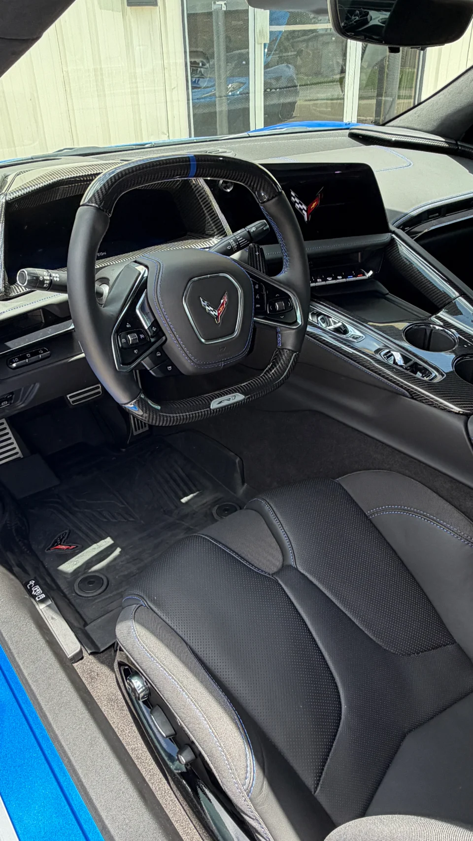 Detailed interior shot of a Corvette C8, featuring a carbon fiber steering wheel with blue accents and black leather seats.