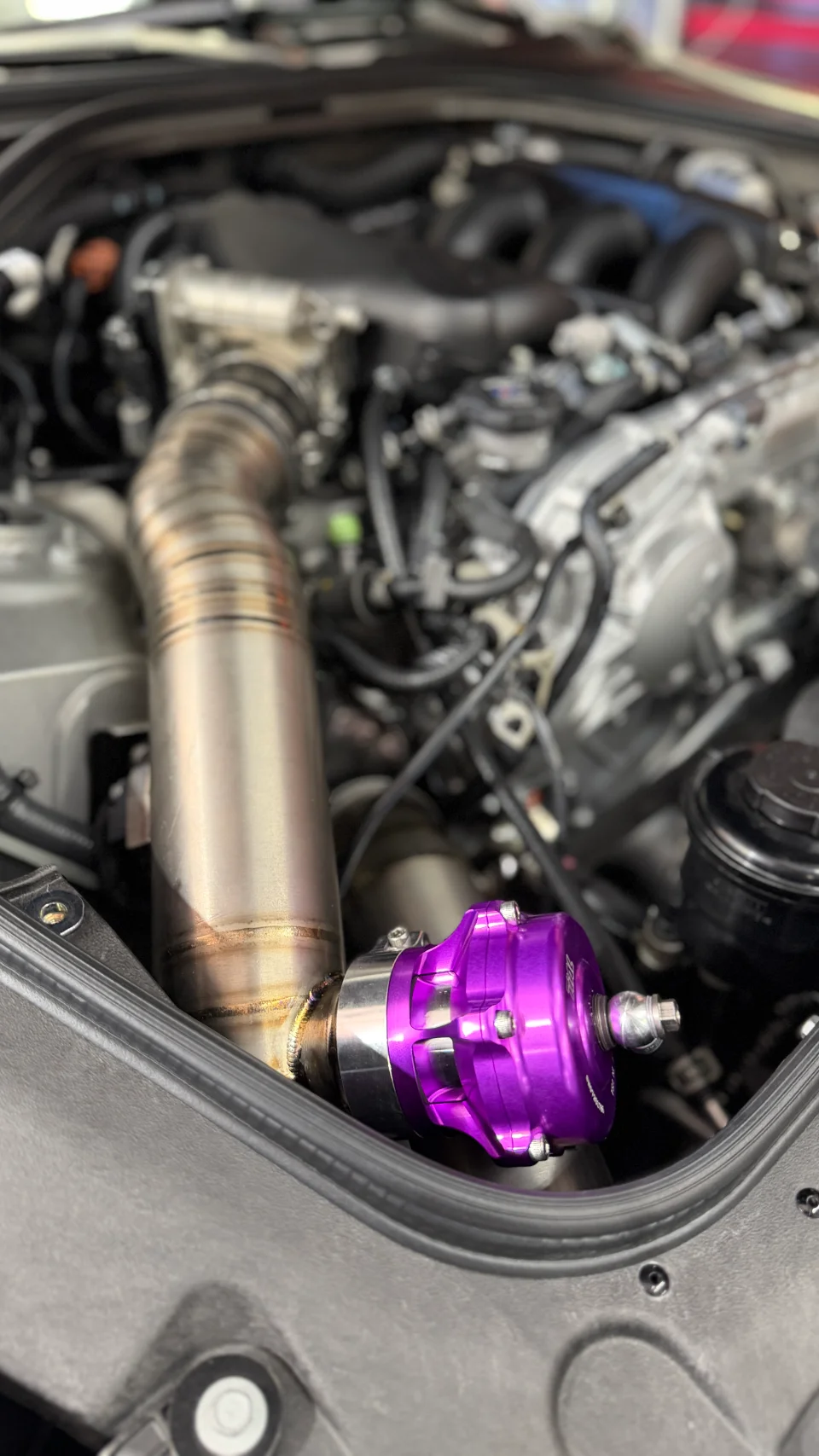 A close-up view of a car's engine bay showing a purple blow-off valve and custom titanium boost piping.