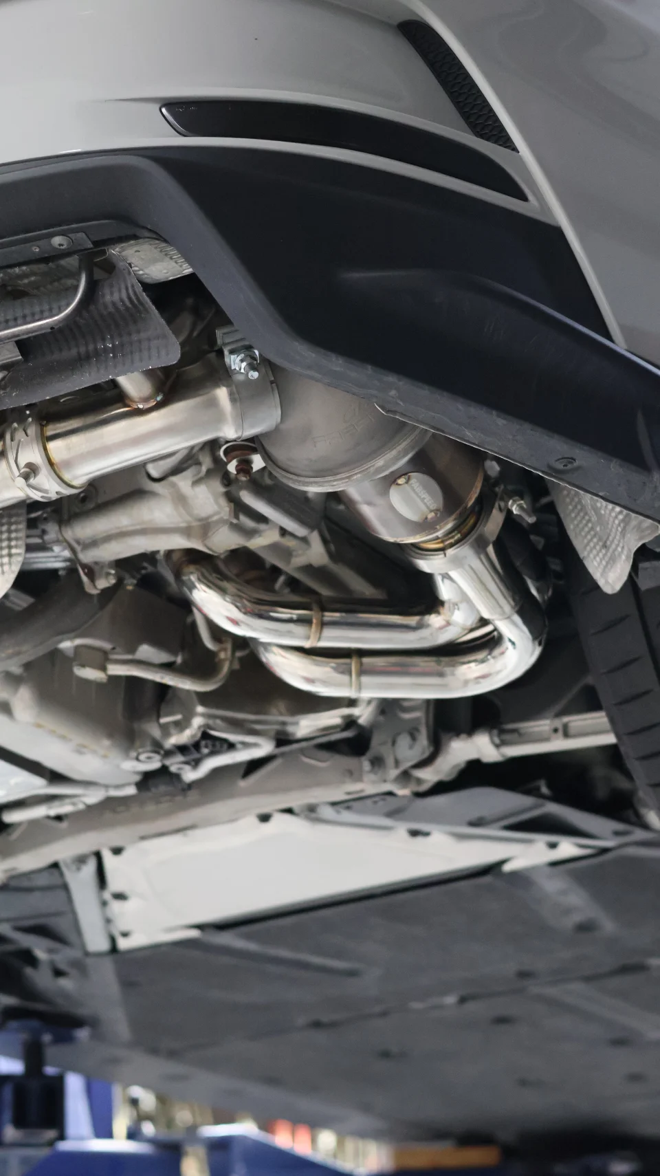Underside view of a performance car on a lift, showcasing a Fabspeed stainless steel exhaust system.