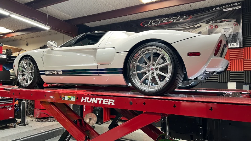 White Ford GT with custom wheels on a red Hunter lift in a performance tuning shop.