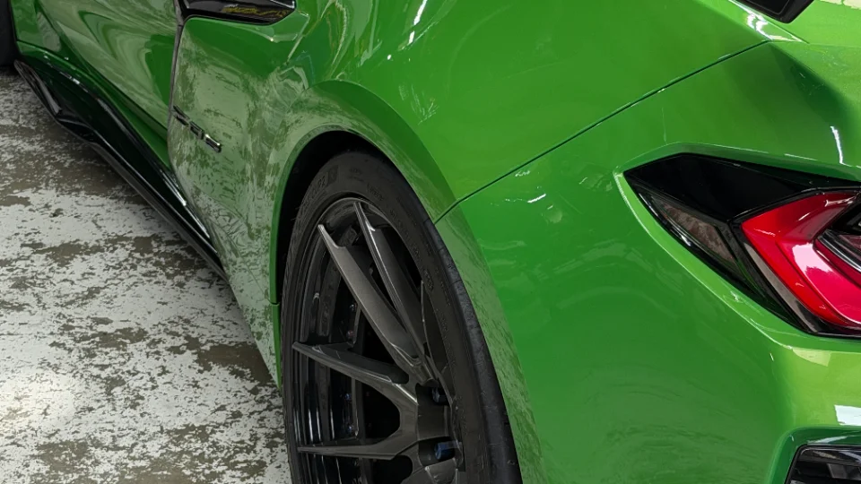 A close-up detail shot of the rear wheel, tire, and side skirt of a vibrant green sports car on a concrete floor.