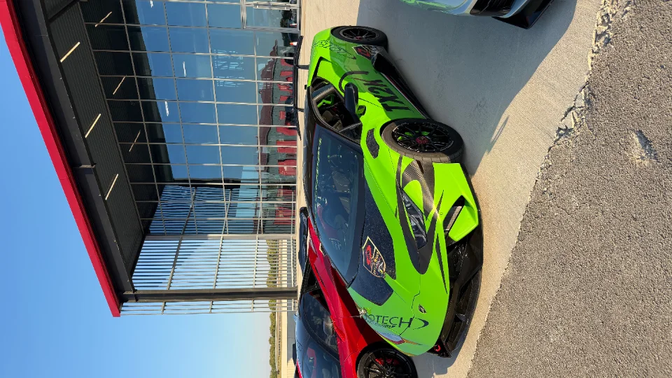 A bright green Lamborghini Huracan with custom Jotech livery and carbon fiber aero parked outside a modern building.