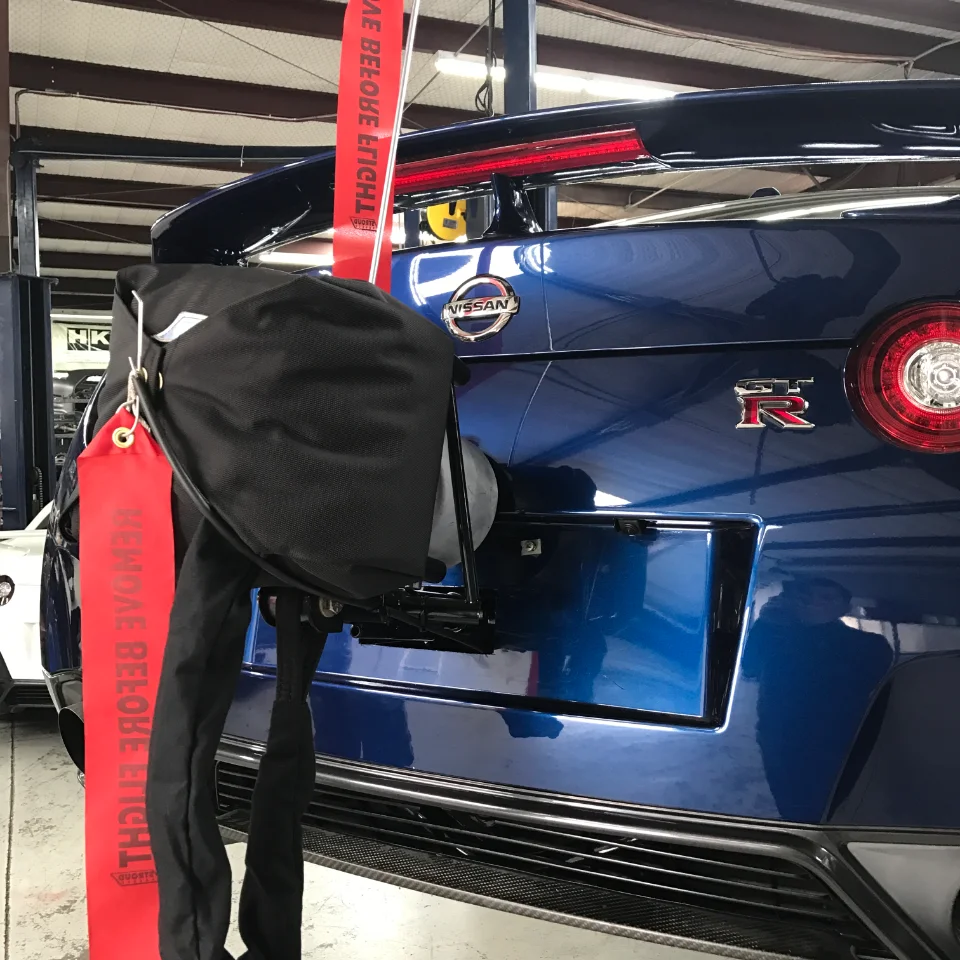 Rear view of a blue Nissan GT-R with a drag racing parachute system installed in a performance shop.