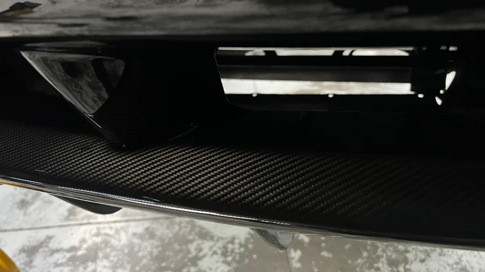 A tight close-up view of a carbon fiber aerodynamic component on a performance car, showing its woven pattern.