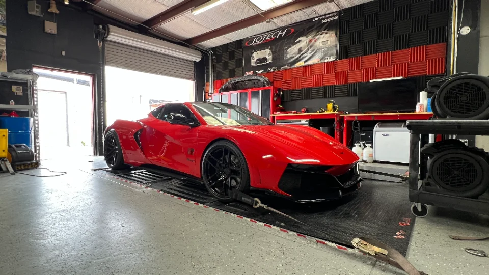 A red supercar, possibly a custom Ferrari or Corvette, strapped to a dynamometer at Jotech Motorsports for performance tuning.