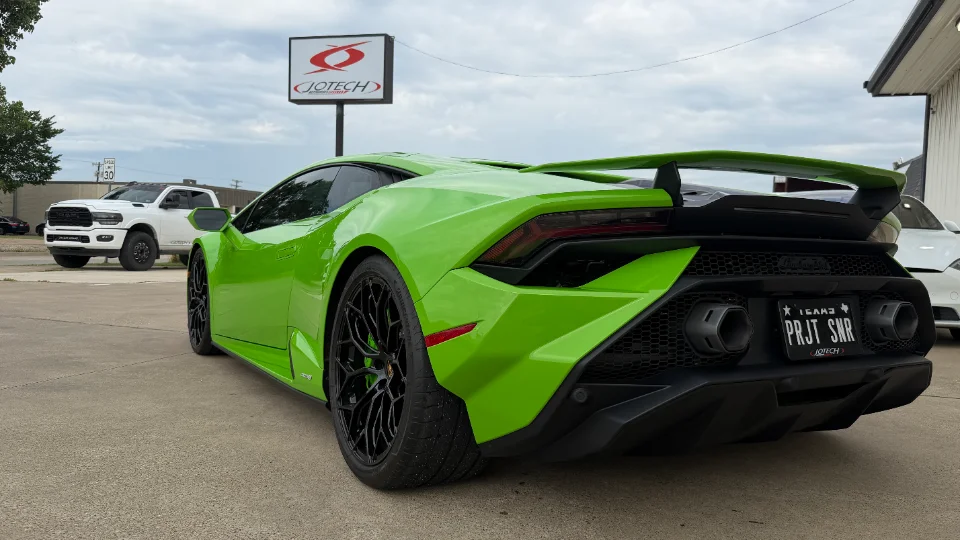 A bright green Lamborghini Huracan with aftermarket wheels and a large rear wing parked outside Jotech Motorsports.