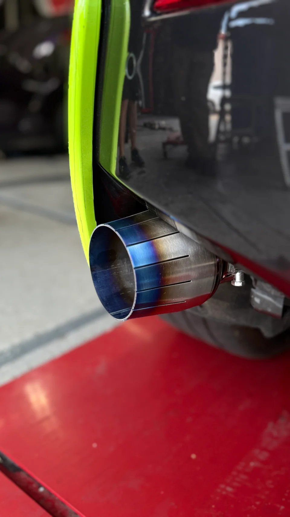 A close-up of a car's aftermarket titanium exhaust tip with a burnt blue finish, installed in a shop setting.