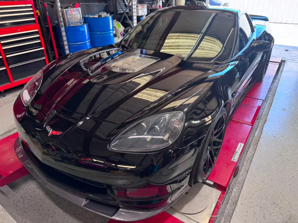 A black C6 Corvette strapped to a red dyno in a performance tuning shop.