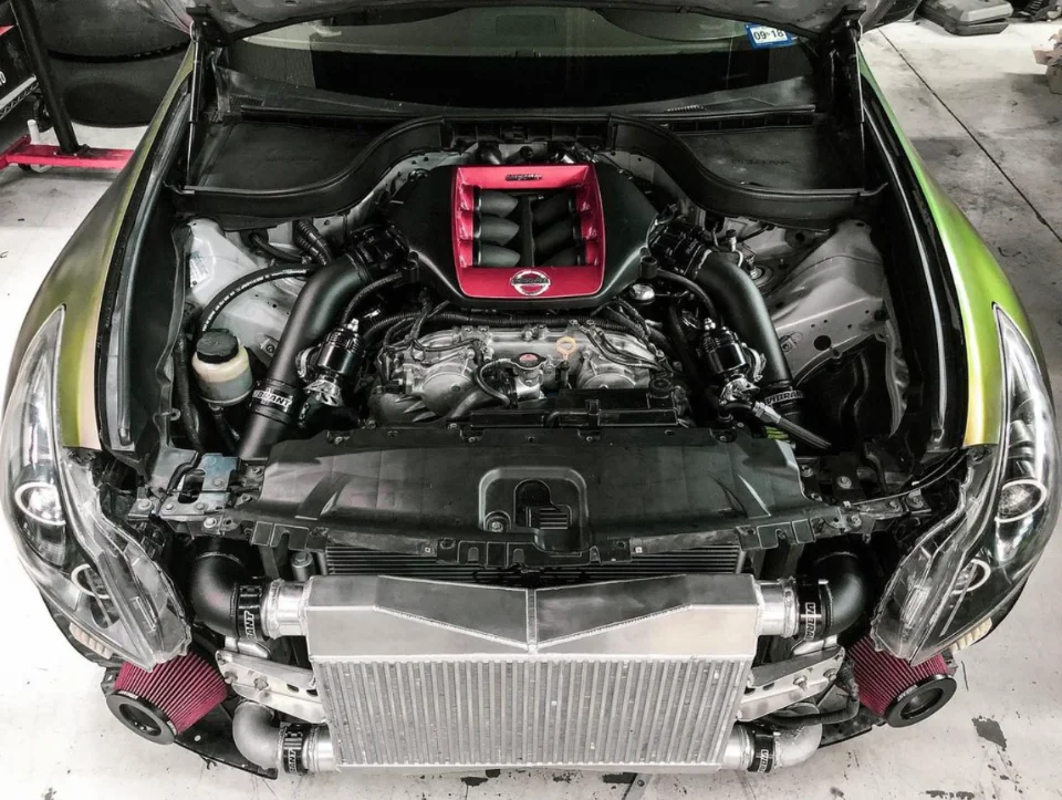Detailed view of a high-performance Nissan/Infiniti engine bay with a large intercooler, custom intake manifold, and red air filters.