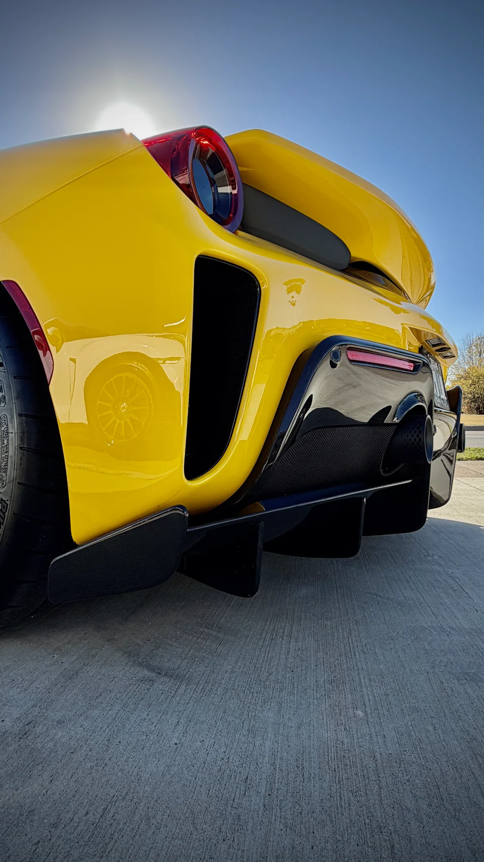 Rear view of a bright yellow Ferrari supercar showcasing its carbon fiber diffuser and exhaust tips under a clear sky.