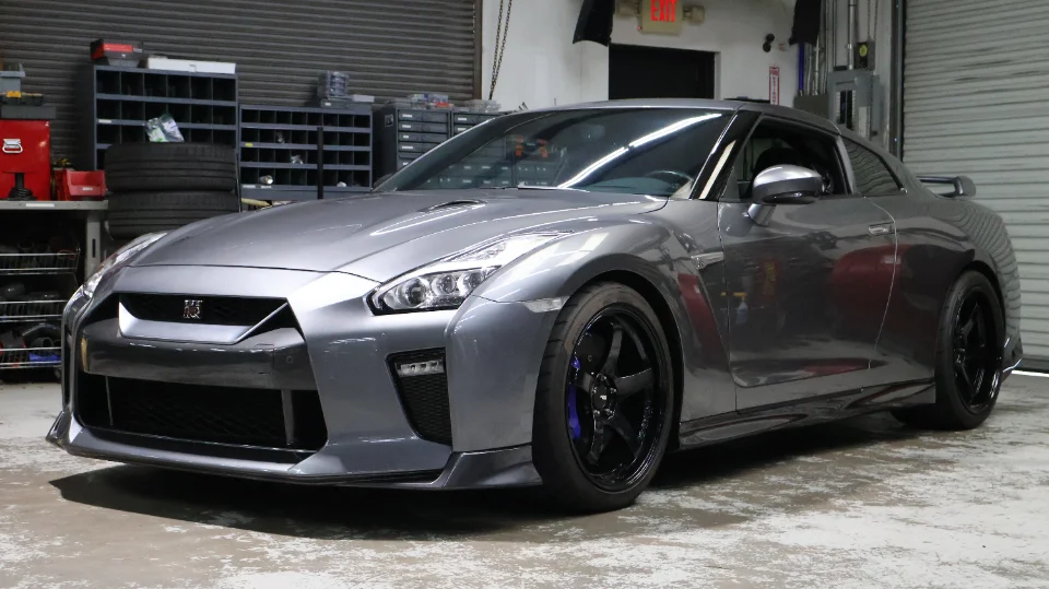 A grey Nissan GT-R R35 with black aftermarket wheels parked inside a performance tuning shop.