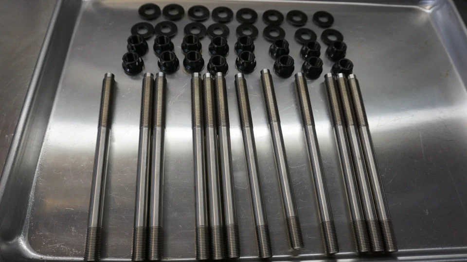 Close-up of new engine studs and nuts laid out on a metal tray in a performance shop.
