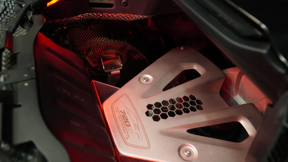 Close-up of a McLaren 720S engine bay, showing the 4.0L twin-turbo V8 and carbon fiber heat shielding.
