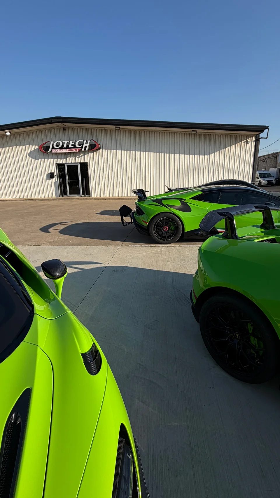 Two vibrant green McLarens parked outside the Jotech Motorsports performance tuning shop on a sunny day.