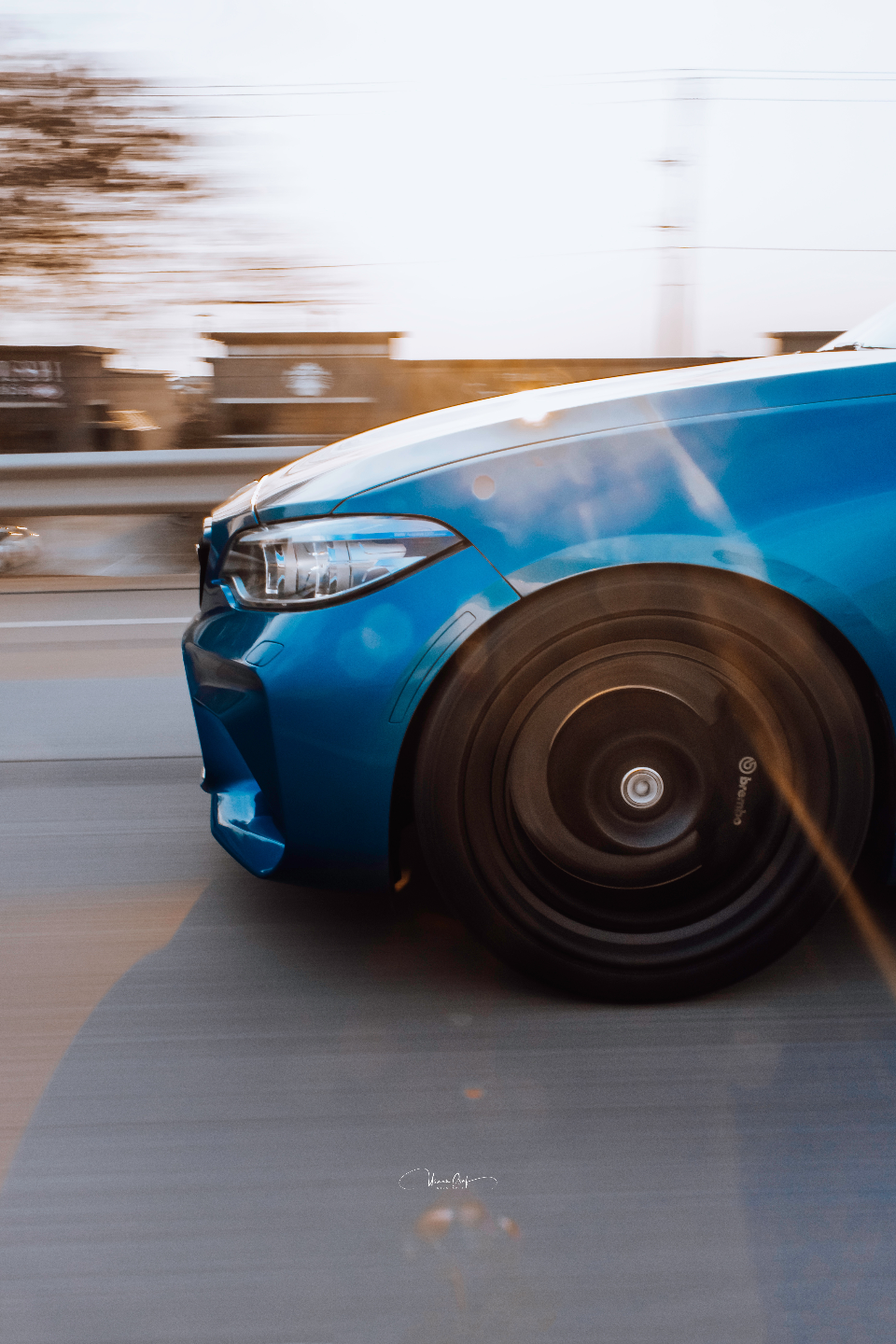 A blue BMW M car in motion, showcasing its front wheel and Brembo brakes with a blurred background.
