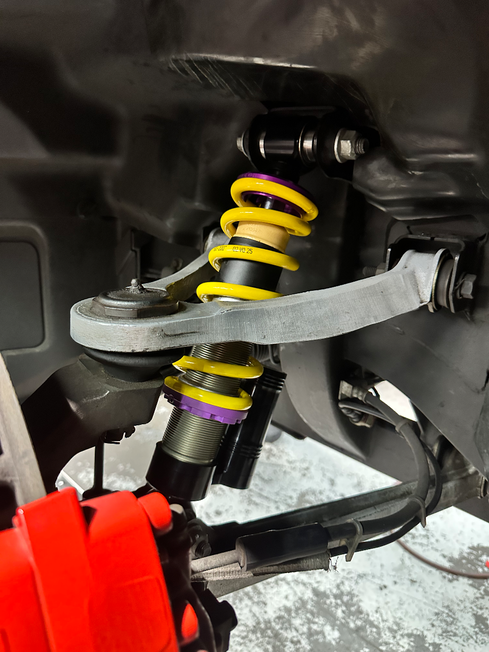A close-up view of KW coilovers and a red brake caliper being installed on a performance car at a tuning shop.